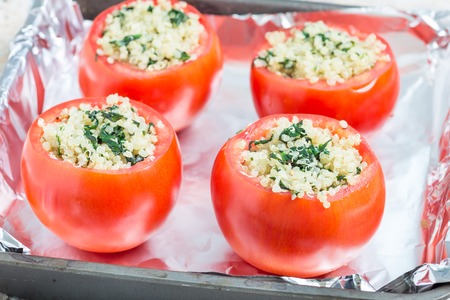 Ready for baking tomatoes stuffed with quinoa and spinach topped with melted cheese in baking dish, horizontal, closeupの写真素材