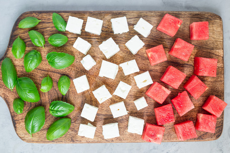 Ingredients for watermelon salad or caprese. Watermelon, feta and basil on a wooden cutting board, horizontal, flat layの写真素材