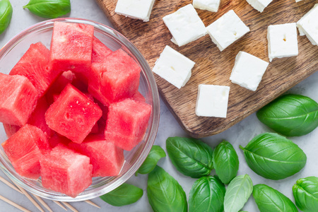 Ingredients for watermelon salad or caprese. Watermelon, feta and basil on a wooden cutting board and in glass, horizontal, flat layの写真素材