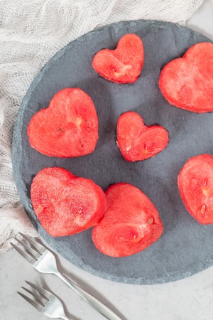 Slices of fresh seedless watermelon cut into heart shape on a slate board, flat lay, vertical