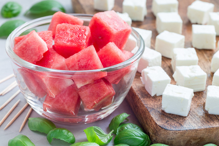 Ingredients for watermelon salad or caprese. Watermelon, feta and basil on a wooden cutting board and in glass, horizontalの写真素材