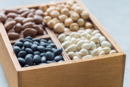 Different kinds of beans: black, pinto, white and chickpeas in a wooden box on concrete background, horizontalの写真素材
