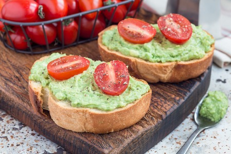 Open sandwiches with mashed avocado and cherry tomatoes on toasted bread, sprinkled with black pepper, horizontalの写真素材