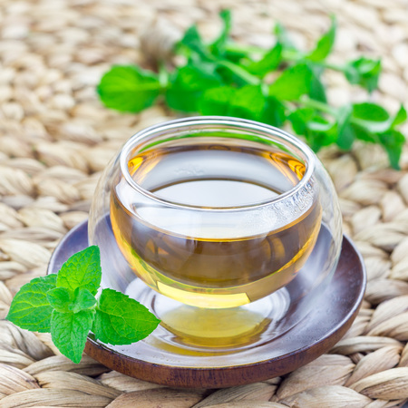 Healthy herbal mint tea in oriental glass cup with fresh peppermint on background, square formatの写真素材