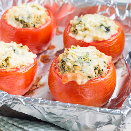 Baked tomatoes stuffed with quinoa and spinach topped with melted cheese in a baking dish, square formatの写真素材