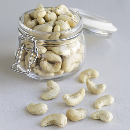 Cashew nuts in glass jar on a light gray concrete background, squareの写真素材
