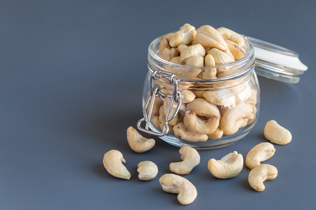 Cashew nuts in glass jar on a dark gray concrete background, horizontal, copy spaceの写真素材