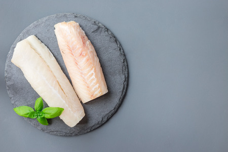 Fresh raw cod fillet with basil on a stone plate, horizontal, copy space, top viewの写真素材