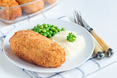Chicken Kiev, ukrainian cuisine. Chicken cutlets in bread crumbs stuffed with butter and herbs, served with mashed potato and green peas, on a white plate, horizontalの写真素材