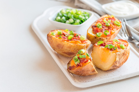 Baked loaded potato skins with cheddar cheese and bacon on ceramic plate, garnished with scallions and sour cream, horizontal, copy spaceの写真素材