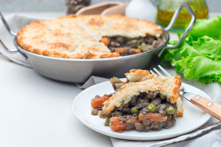 Vegetarian pot pie with lentil, mushrooms, potato, carrot and green peas, covered with puff pastry, on a white plate, horizontal, copy spaceの写真素材