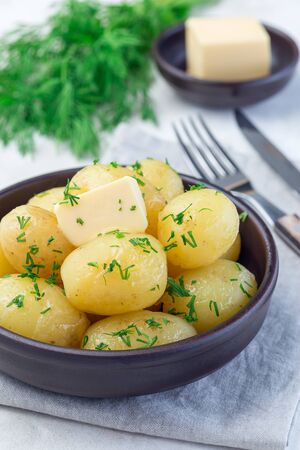 New young boiled potato topped with melted butter and chopped dill in ceramic bowl, verticalの写真素材
