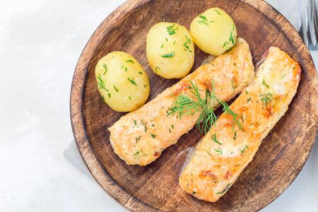 Baked salmon in creamy sauce with young boiled  potato topped with melted butter and chopped dill on  wooden plate, horizontal, top viewの写真素材