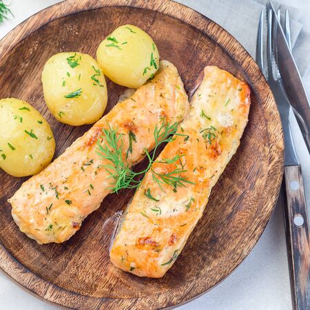 Baked salmon in creamy sauce with young boiled  potato topped with melted butter and chopped dill on a wooden plate, top view, square formatの写真素材