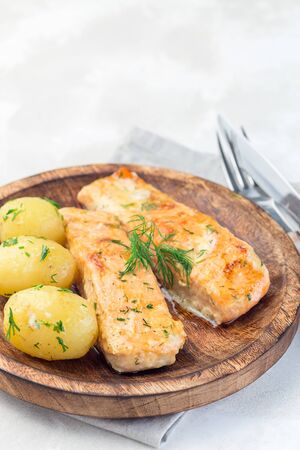 Baked salmon in creamy sauce with young boiled  potato topped with melted butter and chopped dill on a wooden plate, vertical, copy spaceの写真素材