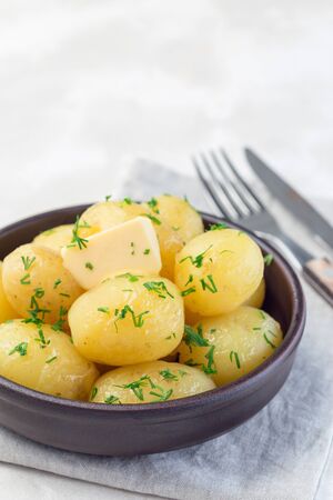 New young boiled potato topped with melted butter and chopped dill in a ceramic bowl, vertical, copy spaceの写真素材