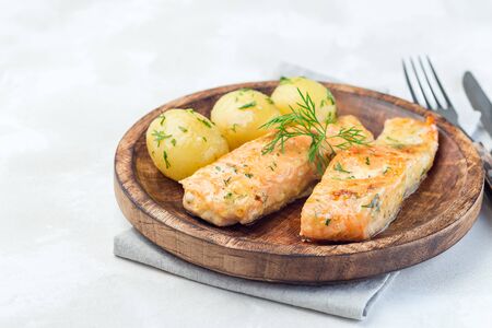 Baked salmon in creamy sauce with young boiled  potato topped with melted butter and chopped dill on a wooden plate, horizontal, copy spaceの写真素材