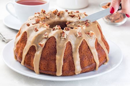 Woman hand with knife cut the sweet potato pecan pound cake with caramel icing,  horizontalの写真素材