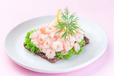 Traditional savory swedish sandwich with a dark bread, lettuce, eggs, mayonnaise, shrimps, dill and lemon, on a pink background, horizontalの写真素材