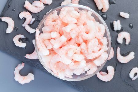 Frozen raw peeled shrimps in a glass bowl on a dark background, horizontal,  top viewの写真素材