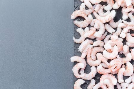Frozen raw peeled shrimps in a glass bowl on a dark background, horizontal, top view, copy spaceの写真素材