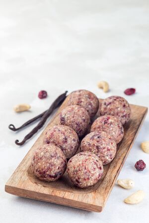 Healthy homemade energy balls with cranberries, cashew nuts, dates and vanilla on a wooden plate, vertical, copy spaceの写真素材