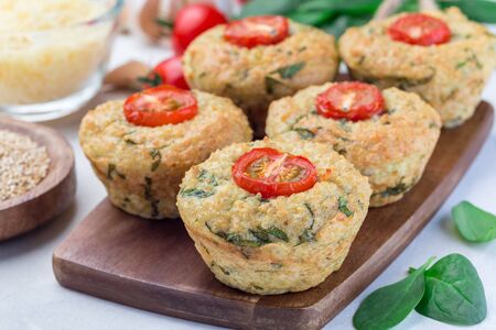 Savory muffins with quinoa, cheese and spinach topped with tomato, on a wooden board, horizontalの写真素材