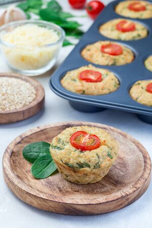 Savory muffins with quinoa, cheese and spinach topped with tomato, on a wooden plate, verticalの写真素材