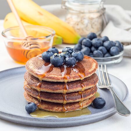 Healthy oatmeal banana pancakes garnished with blueberry and honey, on a gray plate, square formatの写真素材
