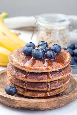 Healthy oatmeal banana pancakes garnished with blueberry and honey, on a wooden plate, verticalの写真素材