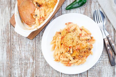 Spicy tomato jalapeno macaroni and cheese with mini penne pasta, in a baking dish and on a plate, horizontal, copy space, top viewの写真素材