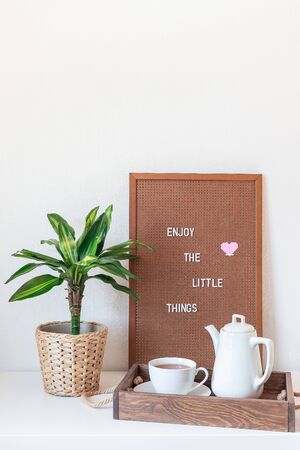 Scandinavian style home interior with white shelves, green palm in  pot, wooden tray with tea, and pegboard with the inspiring phrase, minimalistic concept,  verticalの写真素材