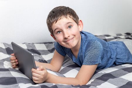 Eight years old boy study or playing at home using a tablet, on a bed