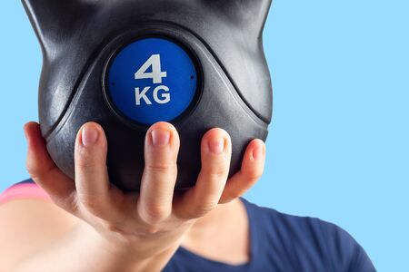 Woman holding heavy dumbbell weights on palm opposite face, isolated on a blue, copy space