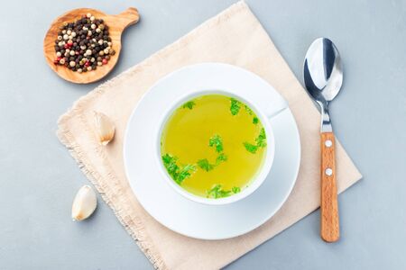 Homemade chicken broth in a white cup garnished with chopped parsley, horizontal, top viewの写真素材