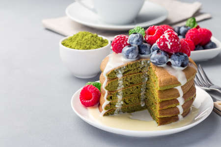 Cuted stack of matcha pancakes served with condensed milk, blueberry and raspberry on a white plate, horizontal, copy spaceの写真素材