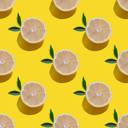 Seamless pattern with hard shadows, half cut lemons with leaves on a yellow background, square formatの写真素材