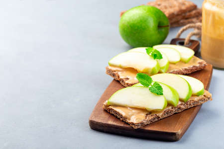 Healthy sandwich with low carb whole grain cracker, green apple slices and peanut butter, on a wooden board, horizontal, copy spaceの写真素材