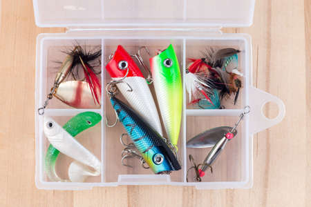 Various fishing lures in plastic box on a wooden background, horizontal, top view