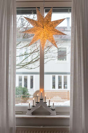 Decorative Christmas  lantern star lamp and lamp with candles or candle bridge on a window, winter time in Sweden,  verticalの写真素材
