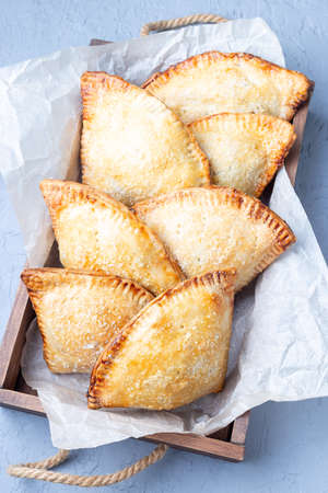 Small peach and cinnamon hand pies with crust dough,  sprinkled with sugar, on a wooden tray,...