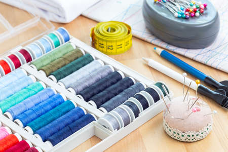 Various sewing accessories, spools and thread, schemes and cloth on a wooden table, horizontal
