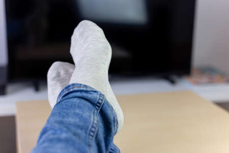 Lazy holidays at home, relaxing woman laying in sofa front of TV, holding her legs on a table,...