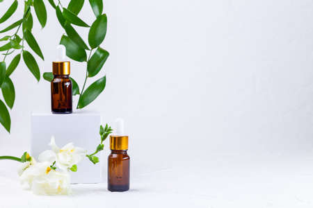 Brown glass pipette bottles with white podium, flowers and green leaves. Organic, natural cosmetic in zero waste eco glass container. Horizontal, copy spaceの写真素材