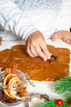Child cuts gingerbread cookies dough with Christmas mold on table, verticalの写真素材