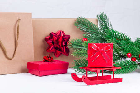 Red gift box on Santa sleigh, Christmas tree branches, gift boxes and bags on background, horizontal