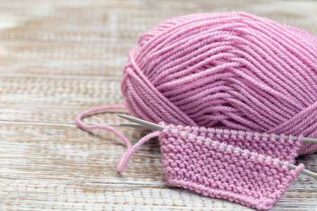 Piece of knitting with needles and pink yarn skein on wooden background, horizontal, copy spaceの写真素材