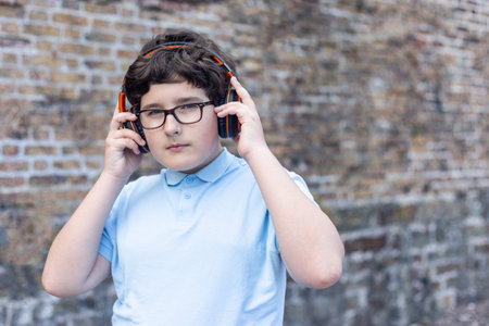 Portrait of eleven years old boy in glasses, wearing wireless headphones, horizontal, copy space