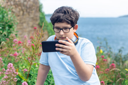 Portrait of eleven years old boy in glasses, watching at smartphone outdoors horizontalの写真素材