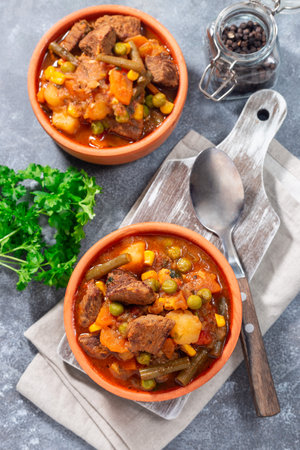 Homemade beef stew with potato, green beans, carrot, peas and corn, in ceramic bowl, vertical, topの写真素材